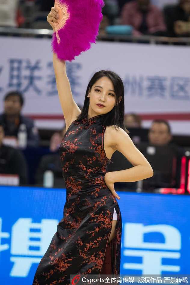 刚柔并济惊艳赛场 江苏肯帝亚啦啦队旗袍扇子舞演绎中国风 在体育馆的背景映衬下,一位啦啦队员轻抚秀发,眉眼含笑,旗袍的温婉与身后巨大的CBA标识形成有趣的视觉对比。