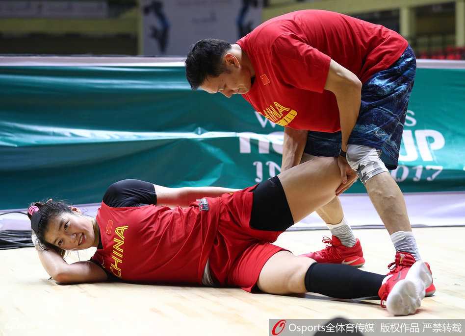 球馆角落，一位印度女保安微笑着注视正在收拾装备的中国女篮队员，队员们则神态自若地整理衣物，气氛安静而融洽。