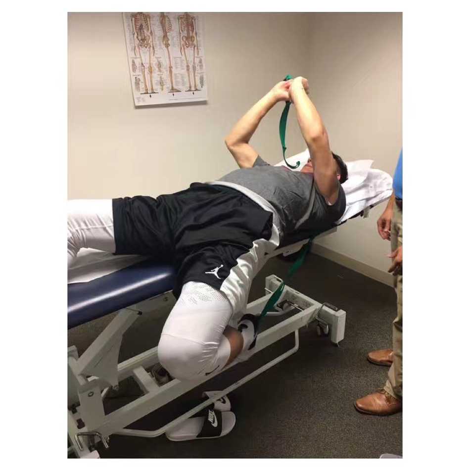 医生正在为可兰白克进行拉伸治疗，他紧咬牙关，小腿肌肉紧绷，虽然面容有些许痛苦，但依然全力配合着康复师的每一个动作。