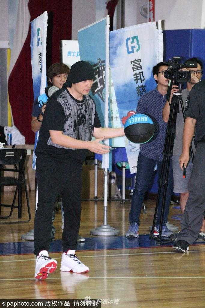 周杰伦站在一架投影钢琴前，面带微笑地挥舞着手臂进行指挥，他身旁的富邦勇士队球星们正用手中的篮球精准地砸向琴键，共同演绎出听妈妈的话的旋律，场面既新奇又温馨。