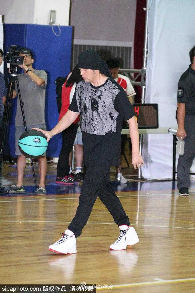 周杰伦在场上指挥跑位，他伸出手臂指向篮筐方向，头巾的结打在脑后，侧脸线条分明，神情专注而认真，完全沉浸在比赛的乐趣中。