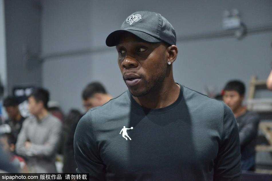 哈德森面带微笑，弯下腰耐心指导一位女球迷运球，眼神专注，场边围满了翘首以盼的观众。