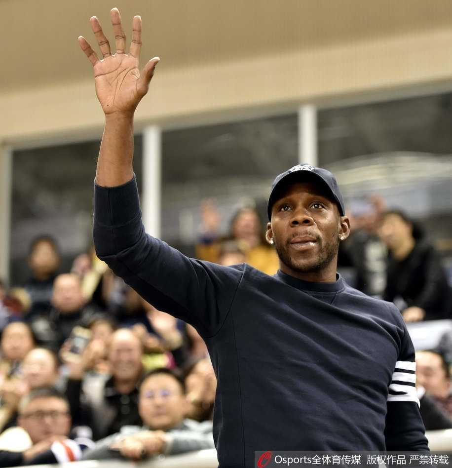 哈德森神情专注地坐在场边，目光紧盯着场内女排队员的激烈对抗，仿佛在战术板上思考着篮球与排球的共通之处。