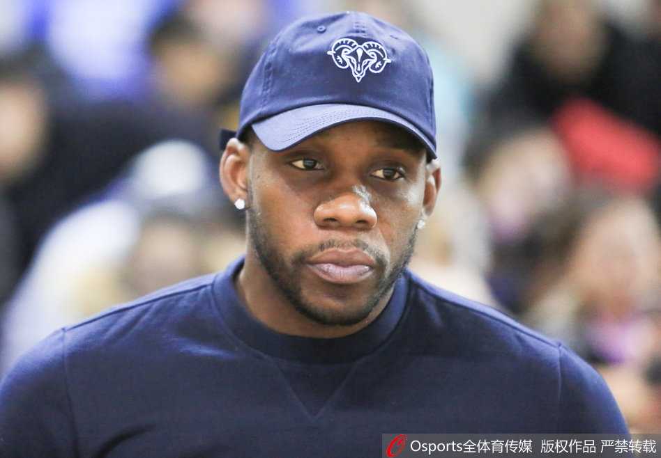 哈德森在场边拿着手机拍摄场内画面，身后是热情的主场球迷，他完全沉浸在女排联赛的热烈氛围中，享受着这个特别的观赛夜晚。