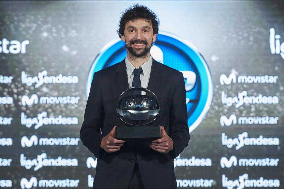 鲁尔手捧西甲MVP奖杯，腼腆的笑容里藏着杀手本色，身后的皇马队旗见证了他这一赛季的传奇。