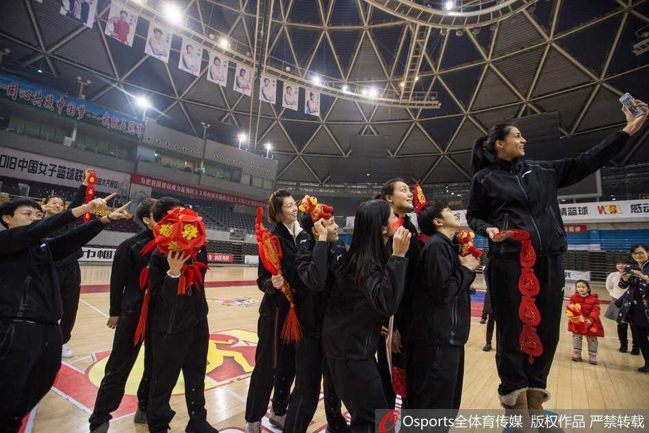 蒂娜·查尔斯露出灿烂笑容，双手捧着一只毛茸茸的狗年吉祥物，仿佛要把这份喜气透过镜头直接递给屏幕前的每一位球迷。