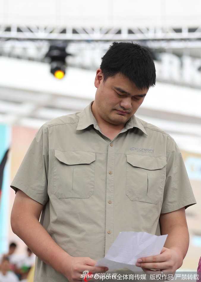 姚明与获胜的中国女篮队员们在赛场边合影留念，高大的他半蹲着与队员们靠拢，画面定格在这一温馨而荣耀的瞬间。