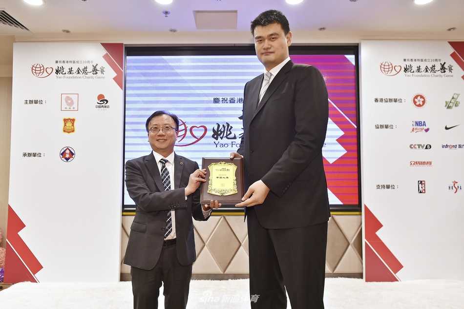 记者招待会现场，姚明正与身旁的一位男士低声交谈，两人神情专注而愉悦，展现了这位篮协主席在严肃公务之外的亲和力与交流热忱。