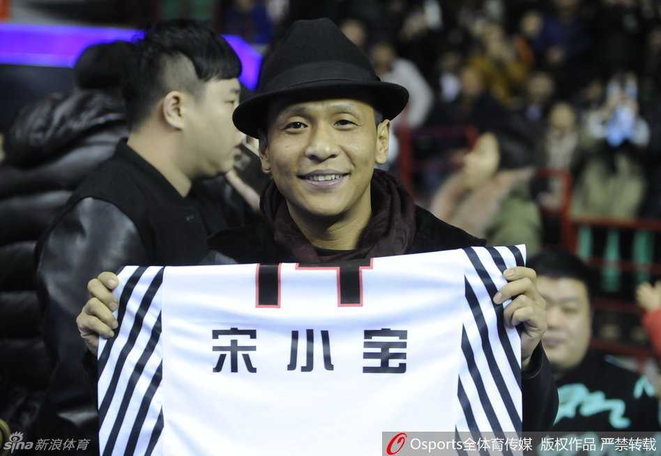 宋小宝双手高举哈德森赠送的14号特别版球衣，站在场边向全场球迷炫耀这份特殊的礼物，表情得意又搞笑，成为全场焦点。