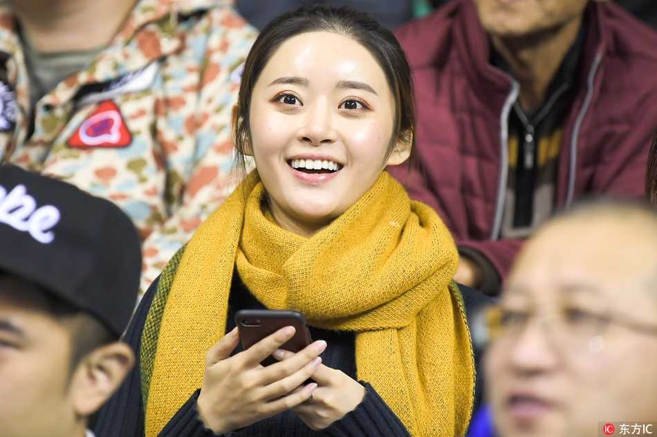 寒冬里的篮球火:本溪主场那些为爱痴狂的美女球迷 一名身穿时尚休闲装的女孩在看台上回眸,背景是欢呼雀跃的人群,她的嘴角带着淡淡的微笑,显得既冷静又迷人。