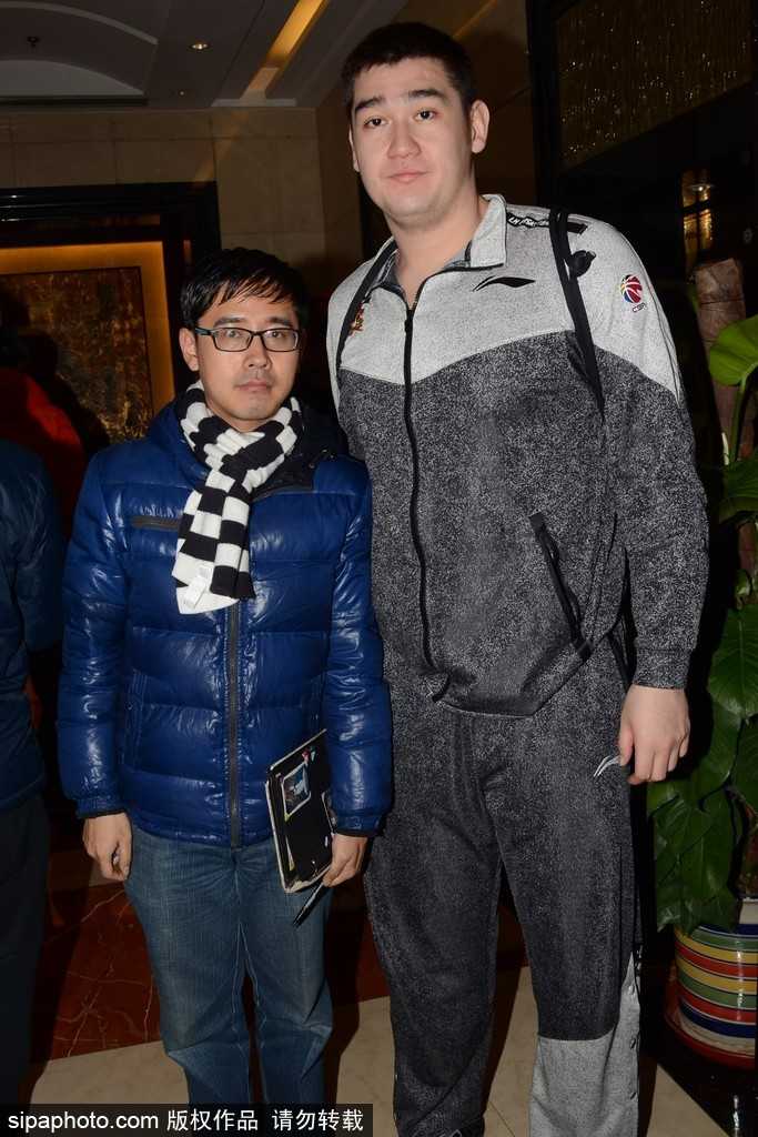 外援琼斯被热情的粉丝团团围住，他一边拉着行李箱缓步前行，一边侧身低头，用记号笔在一位男球迷高举的球衣上留下飘逸的签名，眼神专注而温和。