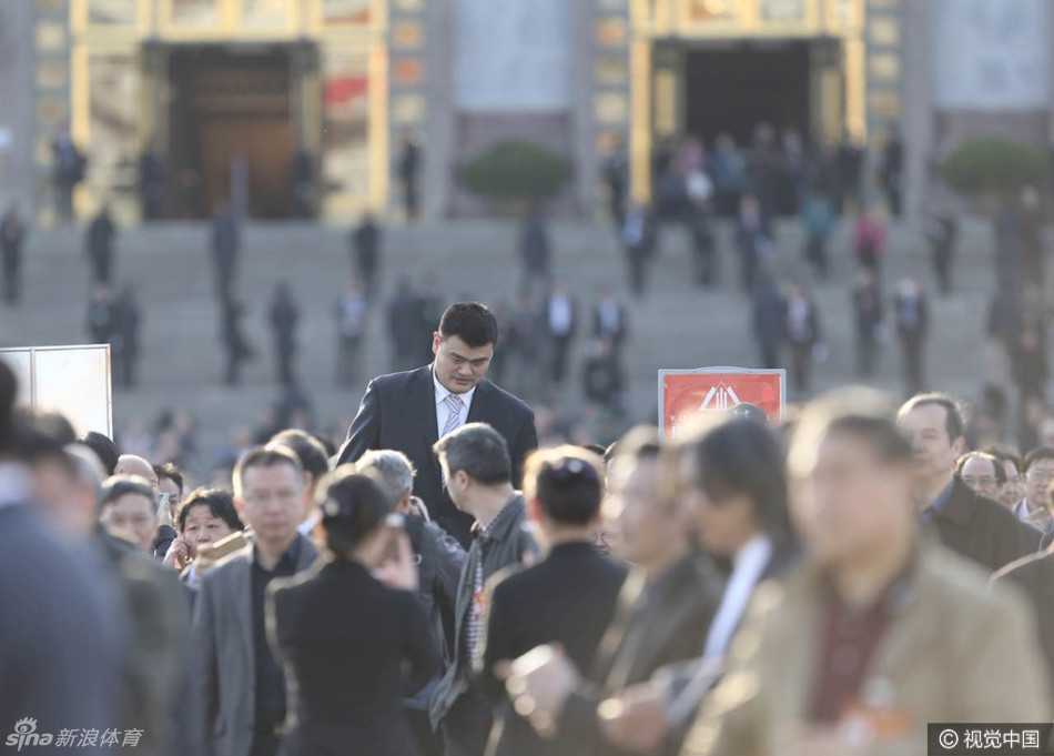 会场外的台阶上，姚明被几位与会者围绕，他们正热切地交谈，姚明微微倾身配合对方，尽显平易近人的风度