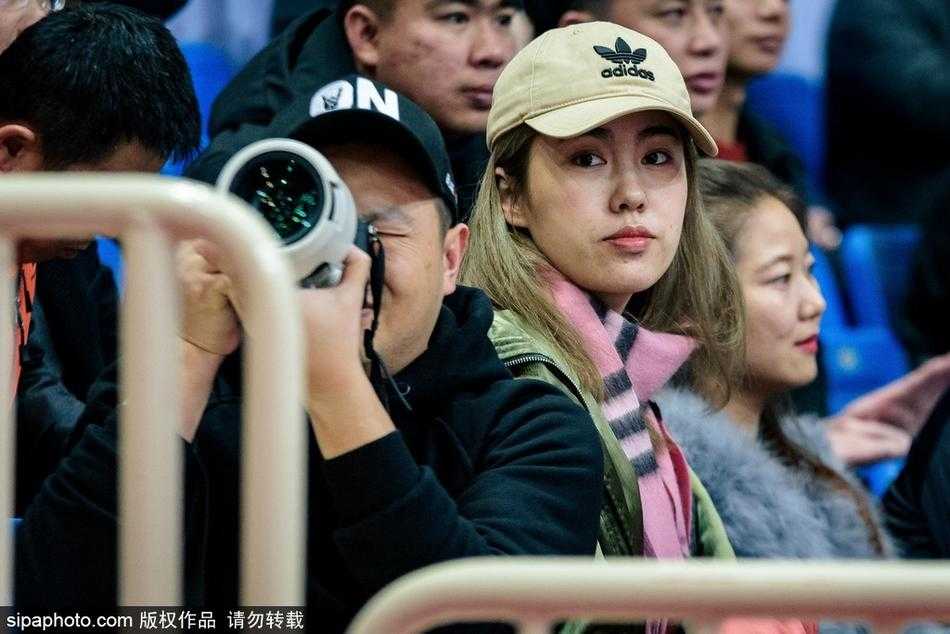 一位身穿浅色衣衫的温婉女子，在喧闹的CBA看台上静静注视着赛场，眼神中透露出对主队局势的担忧与期待，手中的纸杯仿佛也凝固了时间。