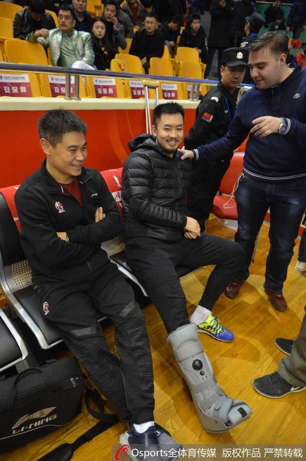 睢冉在场边观战，他双手撑在膝盖上身体前倾，目光紧紧跟随球场上的快攻身影，左脚的护具在昏暗的灯光下显得尤为突出，仿佛诉说着他此刻的无奈。