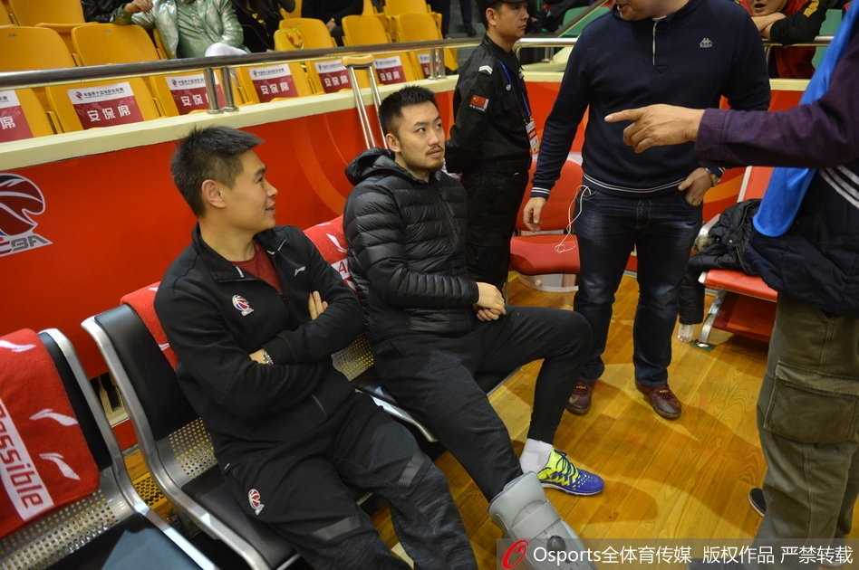 睢冉身穿便服坐在球员替补席上，左脚穿着巨大的保护靴格外显眼，他双手交叉神情专注地看着场内，眼神中透露出焦急与渴望。