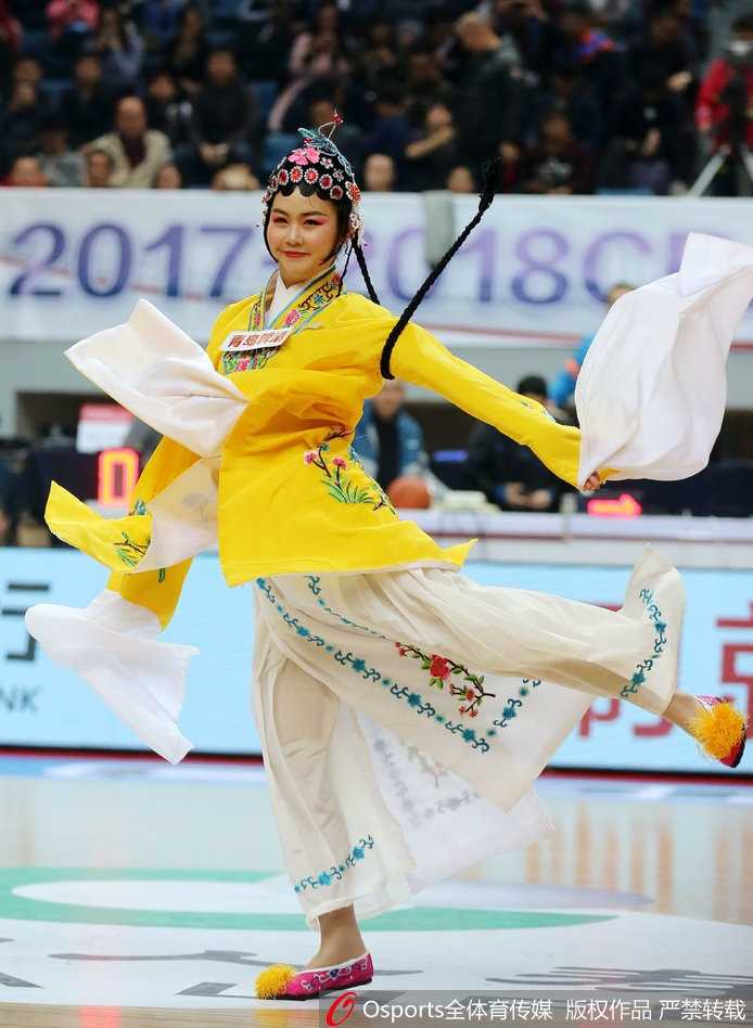 当国粹邂逅篮坛:福建篮球宝贝戏曲服饰演绎别样助威风采 一位篮球宝贝的特写,她身穿粉色的戏曲改良服饰,手举助威花球,在赛场边笑容灿烂,华丽的头饰与现代化的体育场馆形成有趣的视觉对比。