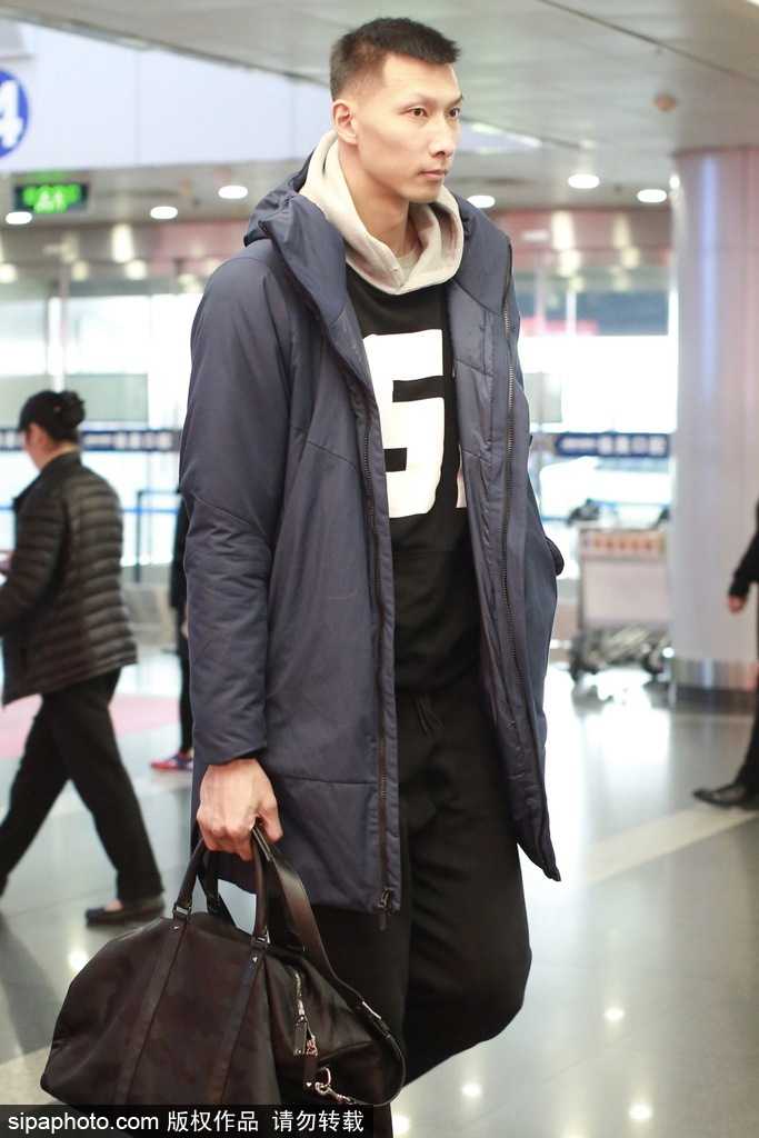 易建联在机场低头查看手机，身上的潮流卫衣图案独特，即使是低头瞬间，挺拔的身姿也让他在人群中格外醒目