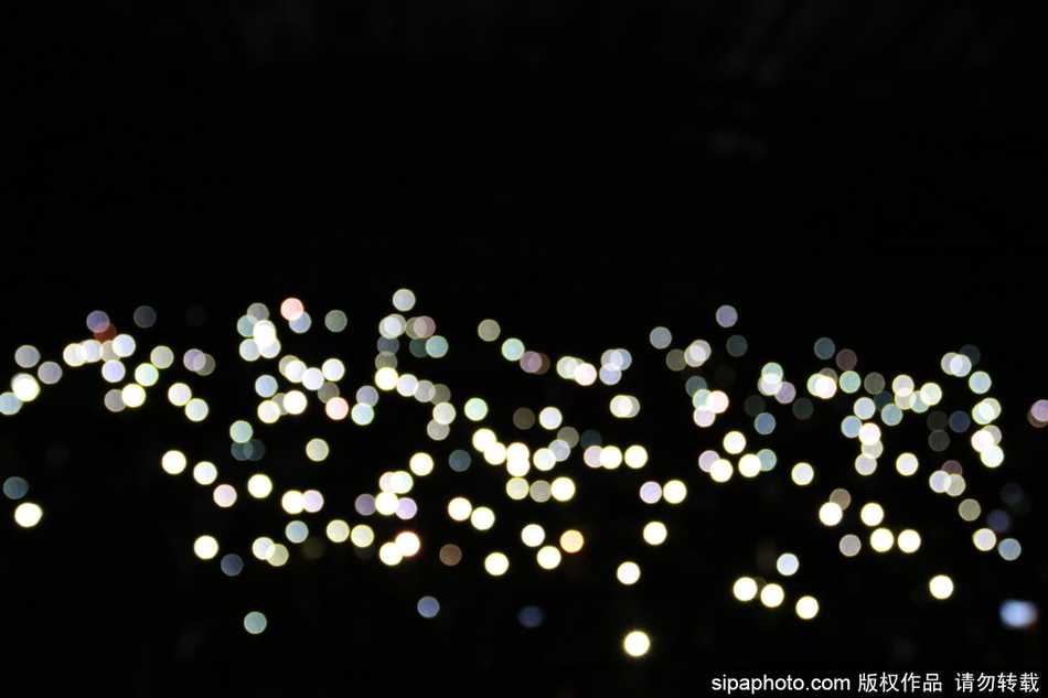 观众们排成一条长龙，正借着手机灯光有序地走向出口，光线在人群中流动，勾勒出一幅互帮互助、文明礼让的画面