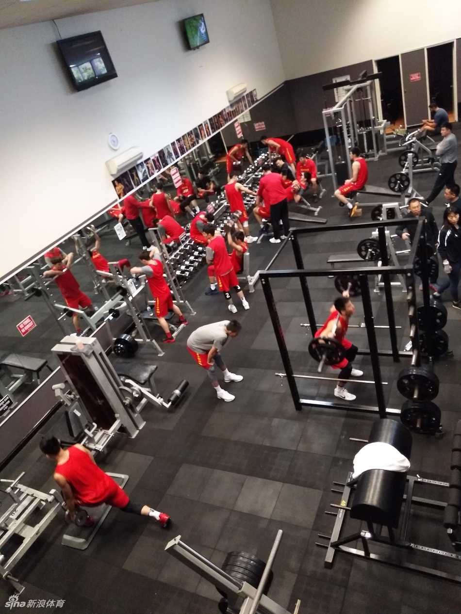 内线支柱韩德君正在进行负重深蹲，庞大的身躯对抗着重力，教练在一旁贴身保护，确保每一个动作都标准到位。