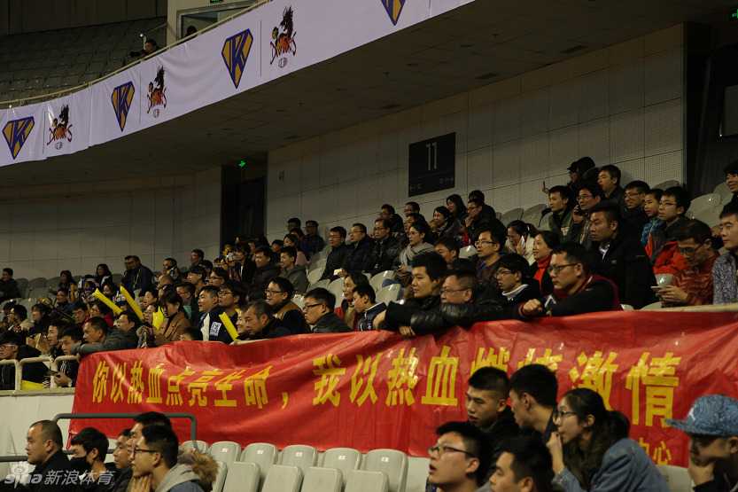 江苏肯帝亚队的主教练兼球员胡雪峰在场边接受媒体采访，他手持话筒，眼神坚定，身后是情绪高涨的球迷看台。