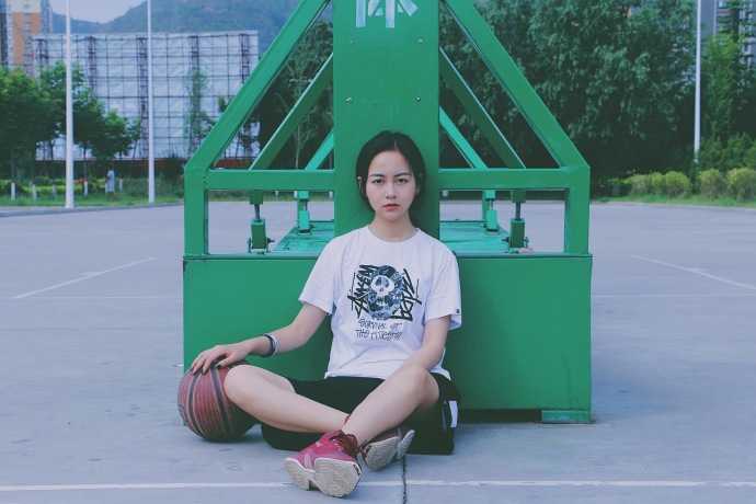 孙夕雨身穿休闲运动背心，头戴棒球帽，手拿篮球站在球场边，眼神清澈明亮，展现出邻家女孩的运动活力。