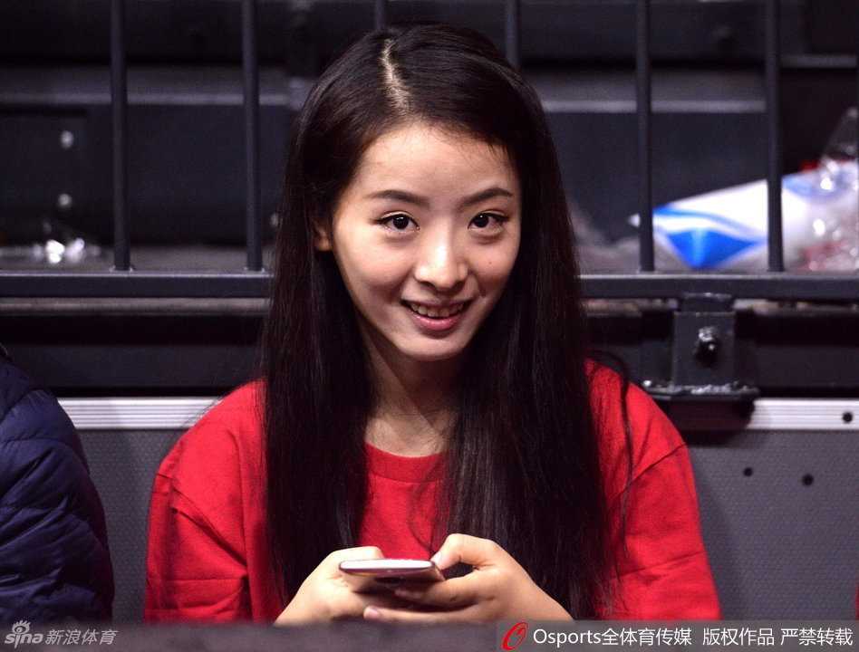 孙桐林的妻子身着优雅便装，目光温柔地追随者球场上的丈夫，嘴角藏着一丝不易察觉的紧张与期盼。