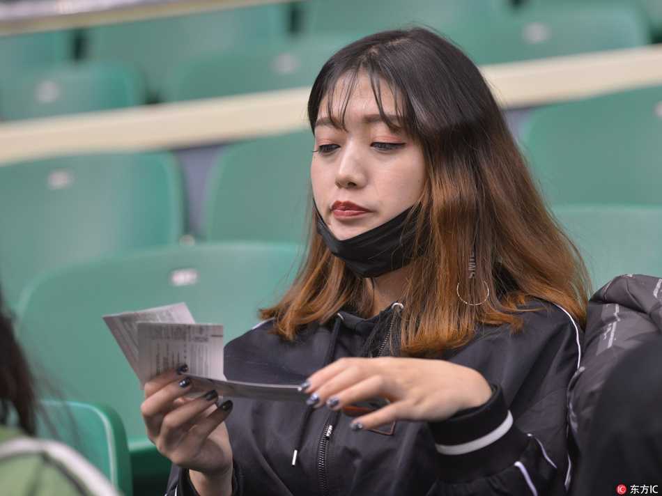 球场灯光下，一位妆容精致的女球迷托腮沉思，眼神中透露出对比赛局势的担忧与期待，仿佛自己就是场边指挥的第十二人。