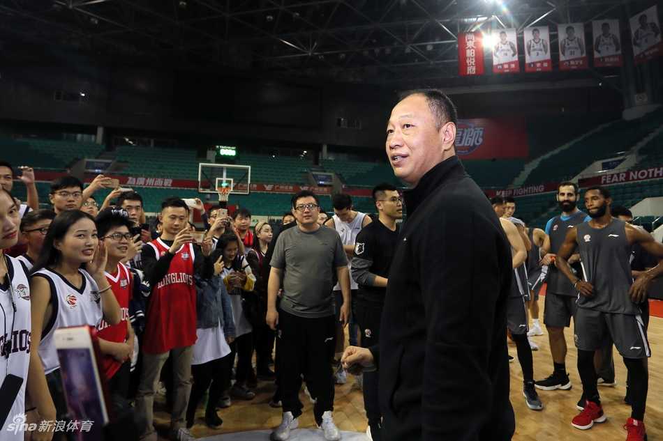 羊城冬日里的热血相聚:广州男篮球迷开放日侧记 广州龙狮男篮开放日现场,球迷们围坐在场边,专注地看着场地中央正在进行的训练,背景是明亮的篮球馆和悬挂的旗帜。