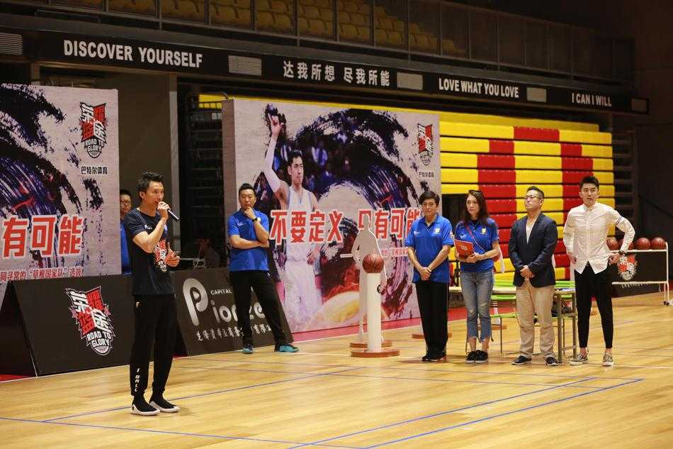 荣耀篮途深圳站:热血激战正酣,十四强进军全国总决赛 晋级十四强的队伍围成一个圈,手臂搭着彼此的肩膀,齐声怒吼庆祝,汗水在灯光下闪闪发光,背景是渐渐落下的夕阳和仍在收拾器材的工作人员。