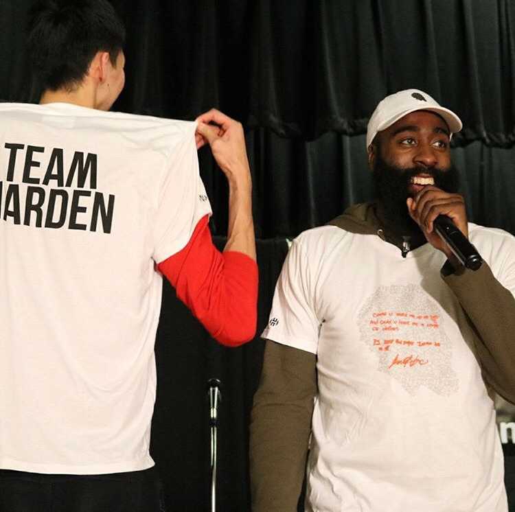 融入·感恩:周琦与哈登阿里扎的休城温情时刻 周琦身穿灰色T恤,在哈登与阿里扎的注视下,专注地手持餐勺为市民盛菜,脸上洋溢着略带羞涩的笑容。