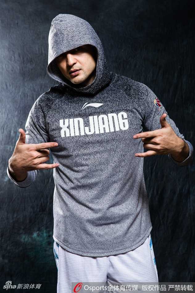 西热力江的嘻哈战袍:新疆后卫的霸气写真与揭幕战传奇 西热力江坐在椅子上身体前倾,双手交叉,身着时尚运动装,表情严肃而富有攻击性,如同场上指挥交通的组织后卫