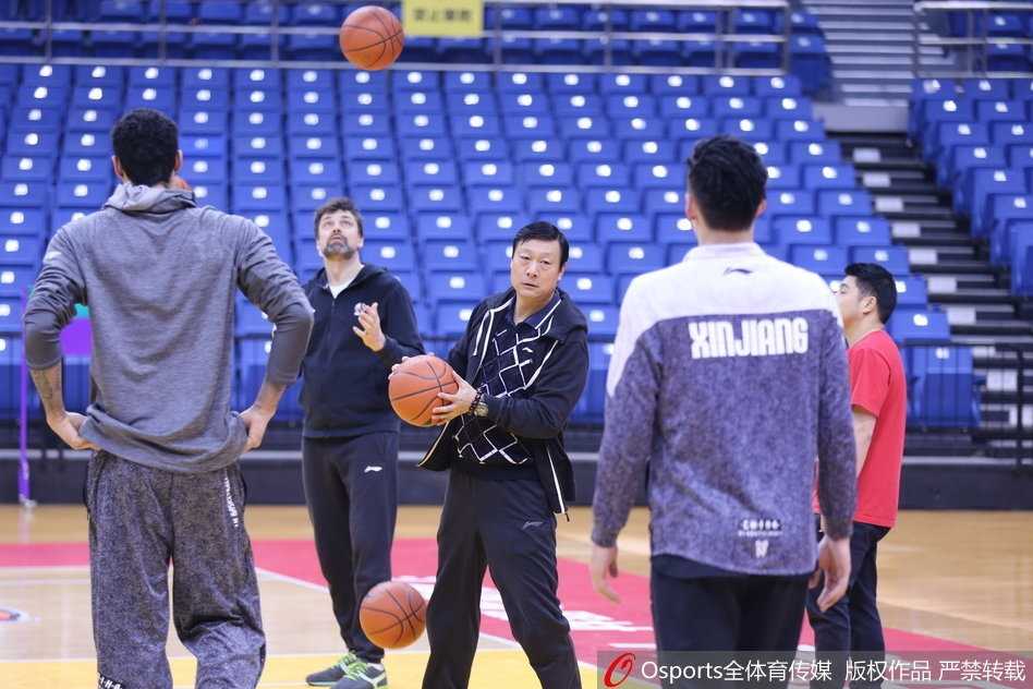 新疆队训练全景，球员们围成一圈听教练布置战术，西热力江站在其中表情认真。