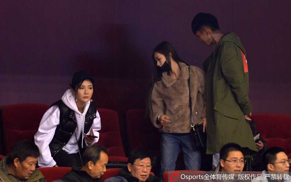 睢冉妻子带着温柔的笑意看向赛场，一旁的丁彦雨航女友则略显青涩，双手轻握，两人的状态放松而自然。