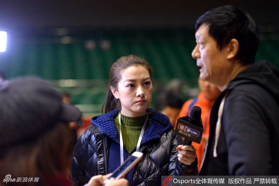 全景镜头下，山东男篮的队员们正在进行快攻上篮练习，篮球在空中划出弧线。美女记者站在场边的摄影位，与身后巨大的球队标志相映成趣，展现出职业体育报道的规范与热情。