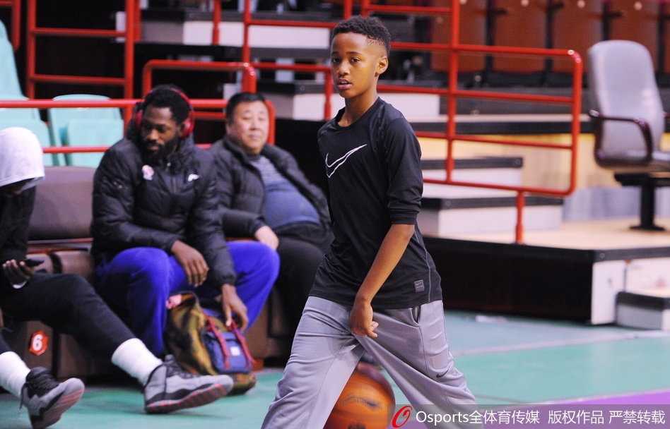 辽宁男篮赛前现温馨一幕 巴斯爱子场边秀球技 巴斯儿子双手举着篮球准备投篮,动作有模有样,巴斯在场边微笑观看