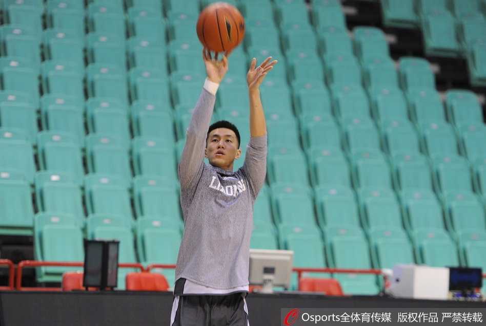 辽宁男篮赛前现温馨一幕 巴斯爱子场边秀球技 巴斯妻子抱着儿子站在场边,一家三口其乐融融,背景是训练中的辽宁队