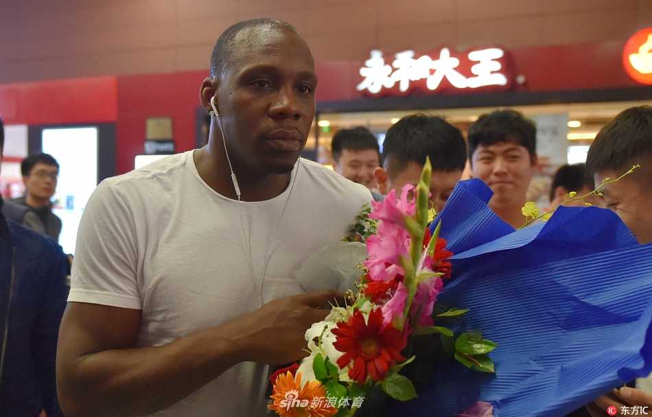 辽篮功勋荣归故里 哈德森抵沈开启冲冠新征程 哈德森手推行李车走出通道,目光坚定地望向远方,身旁簇拥着满脸笑容的球迷,背景里隐约可见“欢迎回家”的横幅,氛围热烈而有序。