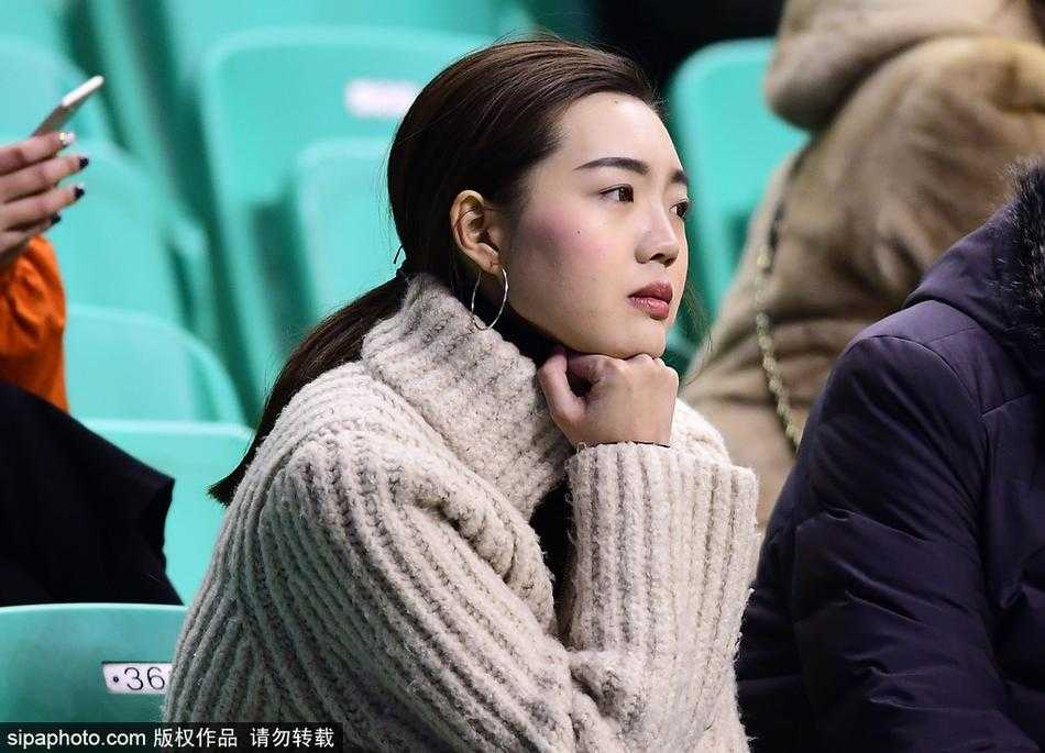 这位辽篮的忠实美女球迷低头微笑，手里拿着助威棒，长长的秀发垂落肩头，整个画面充满了青春的气息，让人感受到赛场边的宁静与美好。