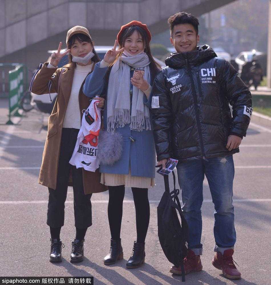 一位身穿白色羽绒服的清秀女球迷，在场馆外安静地守候，眼神中充满了对偶像出现的期待，手中紧握着准备签名的物品。