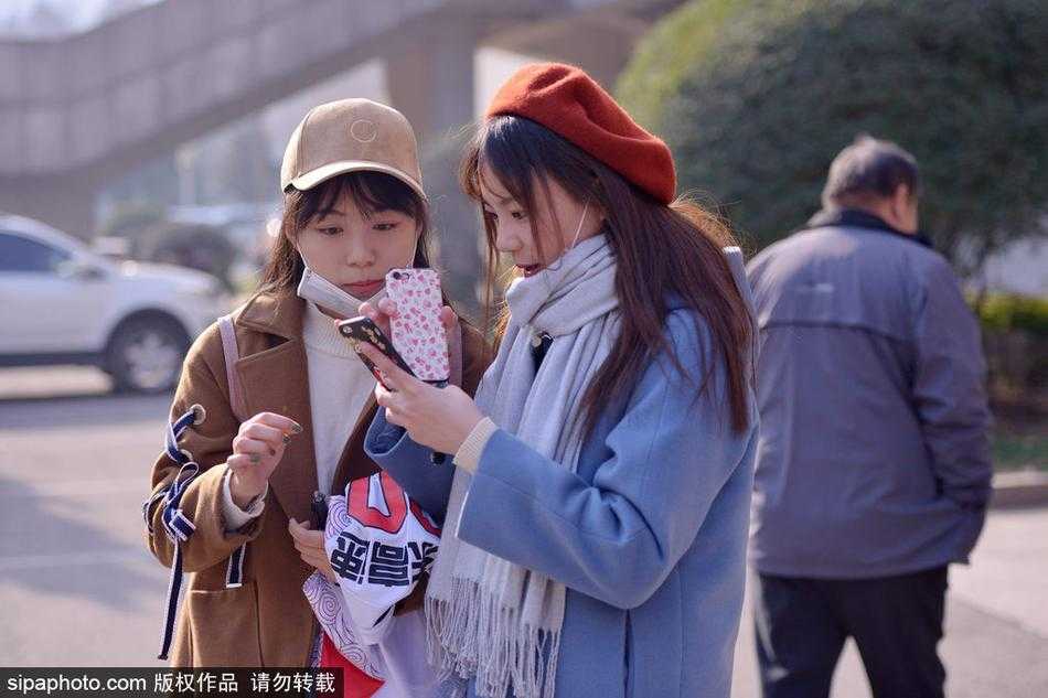 体育馆外的铁栏杆旁，几位年轻的女球迷聚在一起，有的低头摆弄手机，有的则翘首望向场馆内部，她们随身携带的背包上挂着球队的周边饰物。