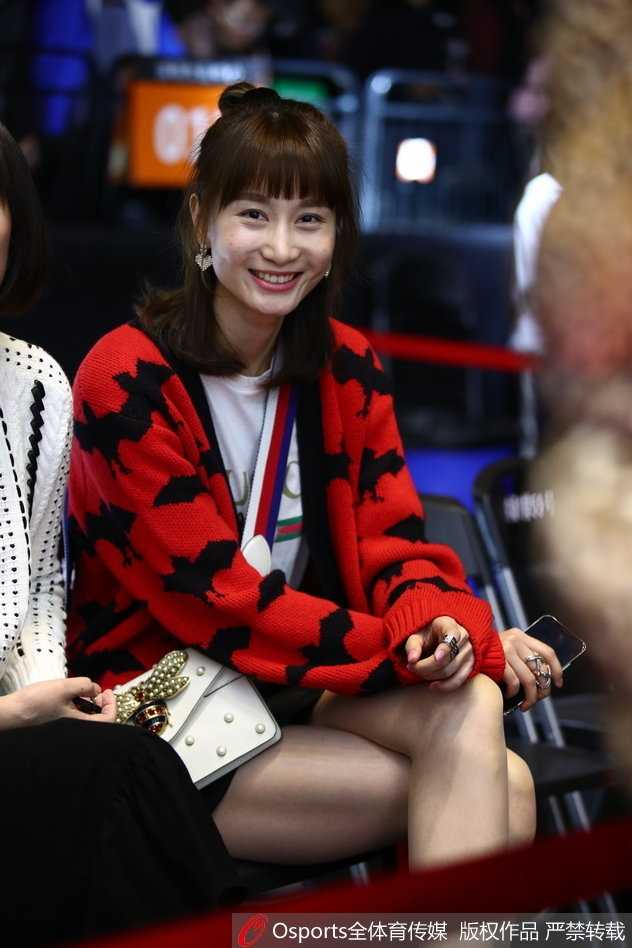 闪耀鹏城:周鹏爱妻领衔太太团助阵,二〇一八CBA全明星赛南区明星队力克北区 这位观战的女士身穿宽松的黑色卫衣,搭配时尚的棒球帽,正用手机自拍记录下这个难忘的全明星之夜,背景是模糊的球场灯光和人海。