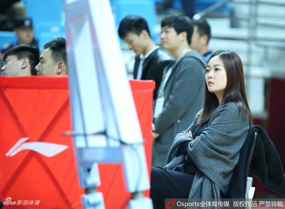 在青岛主场明亮的灯光下，一位戴着眼镜的女球迷回眸瞬间，眼神中透着对比赛的专注与好奇，文艺气息十足