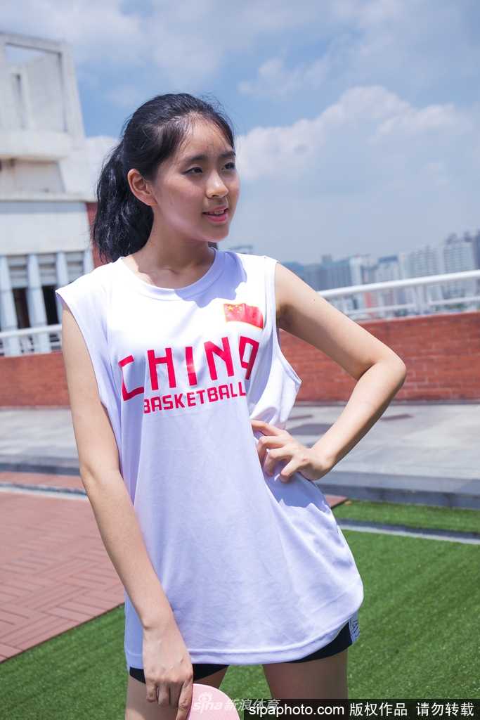青春飞扬:篮球宝贝光影间舞动最美中国力量 女孩身穿白色运动背心搭配牛仔短裤,健康的小麦色肌肤在阳光下泛着光泽,她单手叉腰,身姿挺拔,展现出篮球宝贝特有的自信与健美。
