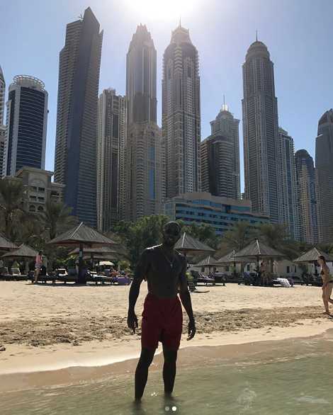 亚当斯身着休闲装，赤脚漫步在迪拜细腻的白色沙滩上，脸上洋溢着轻松惬意的笑容。