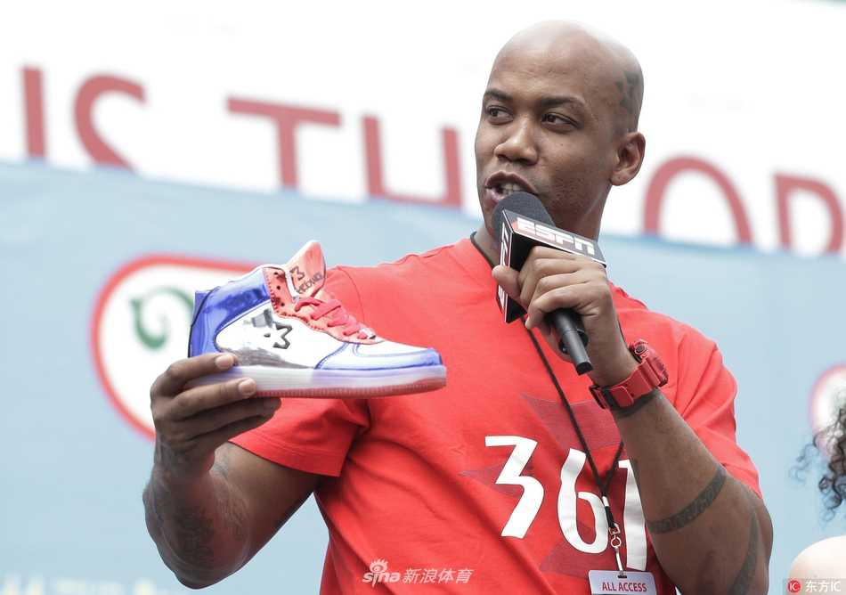 马布里独立日返乡宣传个人品牌 热狗大赛变身移动广告位 马布里现身纽约科尼岛热狗大赛现场,身穿深色紧身运动衣搭配个人品牌球裤,面带微笑望向镜头,背景是熙熙攘攘的围观人群和美国国旗装饰。