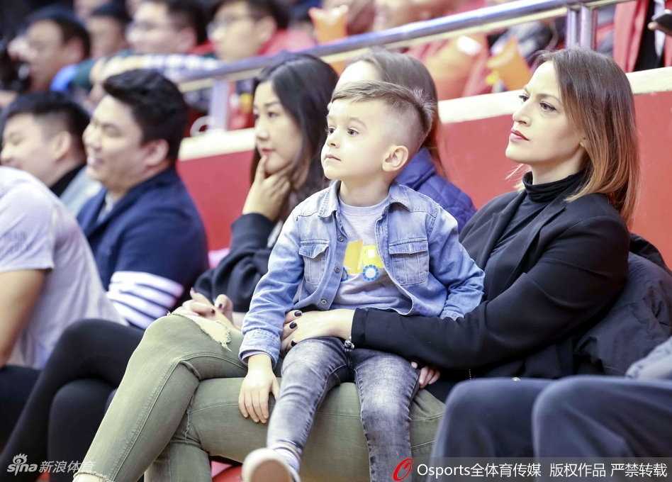 劳森的伴侣身着一袭简约黑衣，倚靠在看台栏杆前，嘴角含笑的她正用手机记录下丈夫在场上组织进攻的指挥官风采。